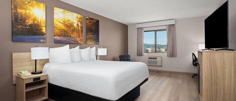 A hotel room with a large bed, a desk, a TV, and two paintings on the wall.
