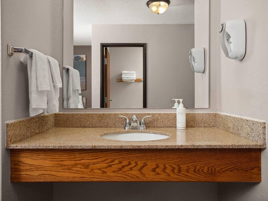 A bathroom with a granite countertop sink, wooden vanity, a mirror, and a towel rack.