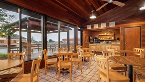 A restaurant with wooden tables and chairs, large windows, and a bar area. - Days Inn by Wyndham Spearfish (Spearfish)