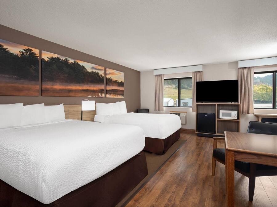 Habitación de hotel con dos camas, televisor, escritorio y vista a un bosque.