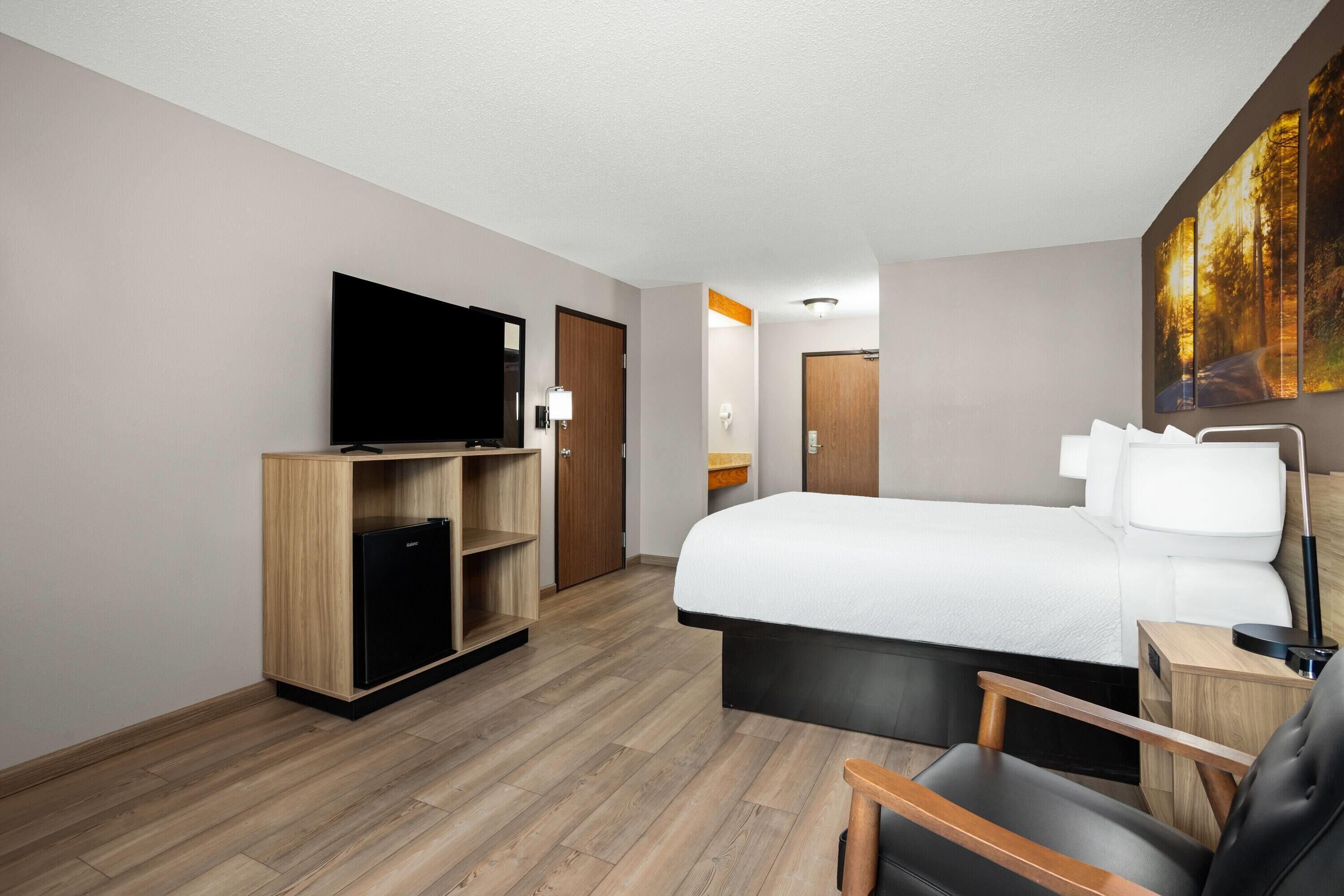 Une chambre d’hôtel avec un grand lit, un téléviseur posé sur une commode en bois, un bureau avec une lampe et un tableau accroché au mur.