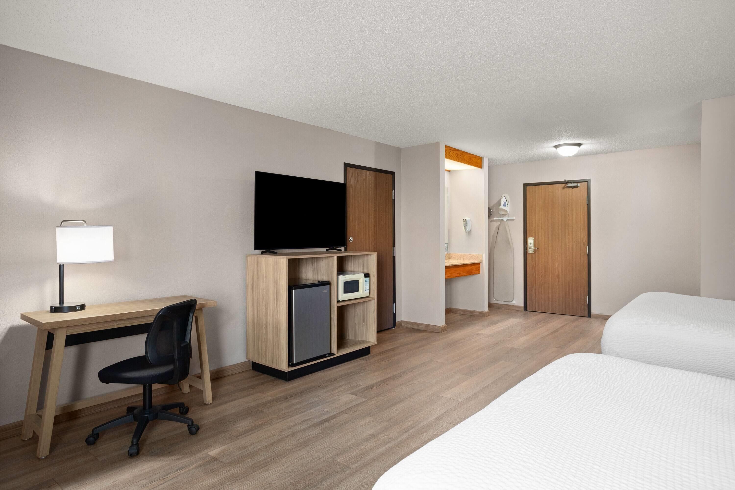 A hotel room with a bed, a desk with a computer, a TV, and a microwave.