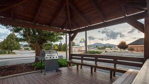A covered outdoor area with a grill, benches, and a view of a road and distant mountains. - Days Inn by Wyndham Spearfish (Spearfish)