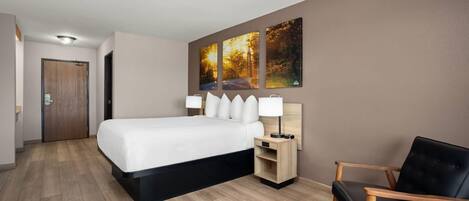 Una habitación de hotel moderna con una cama grande, mesitas de noche, una silla y una obra de arte colgada en la pared.