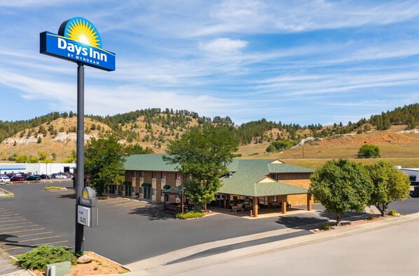 A Days Inn by Wyndham with a parking lot, covered outdoor seating area, and a mountainous backdrop. - Days Inn by Wyndham Spearfish (Spearfish)