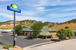 Um Days Inn by Wyndham com estacionamento, área de estar coberta ao ar livre e montanhas ao fundo.