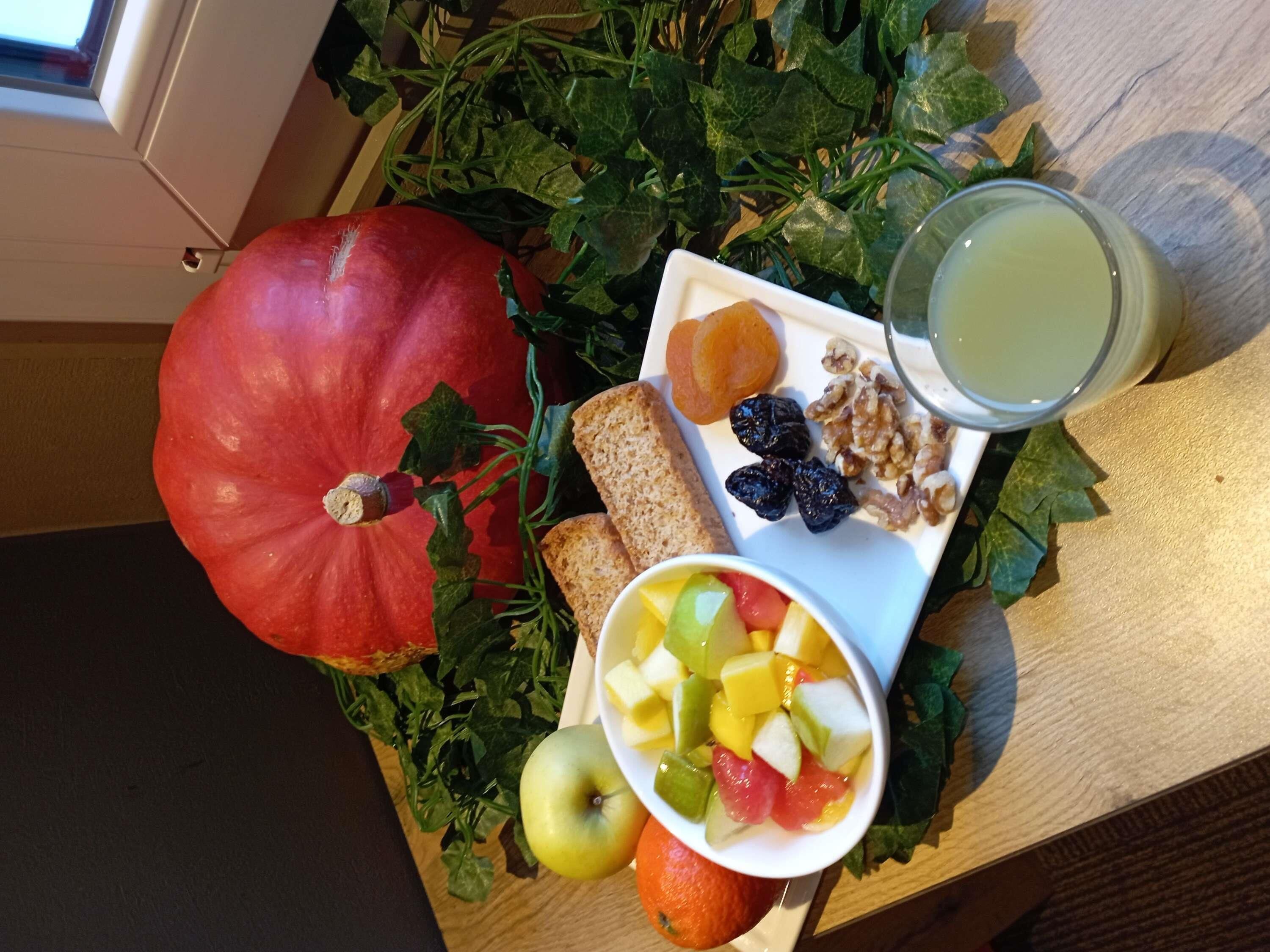 A table with a pumpkin, fruits, nuts, bread, and a glass of juice.
