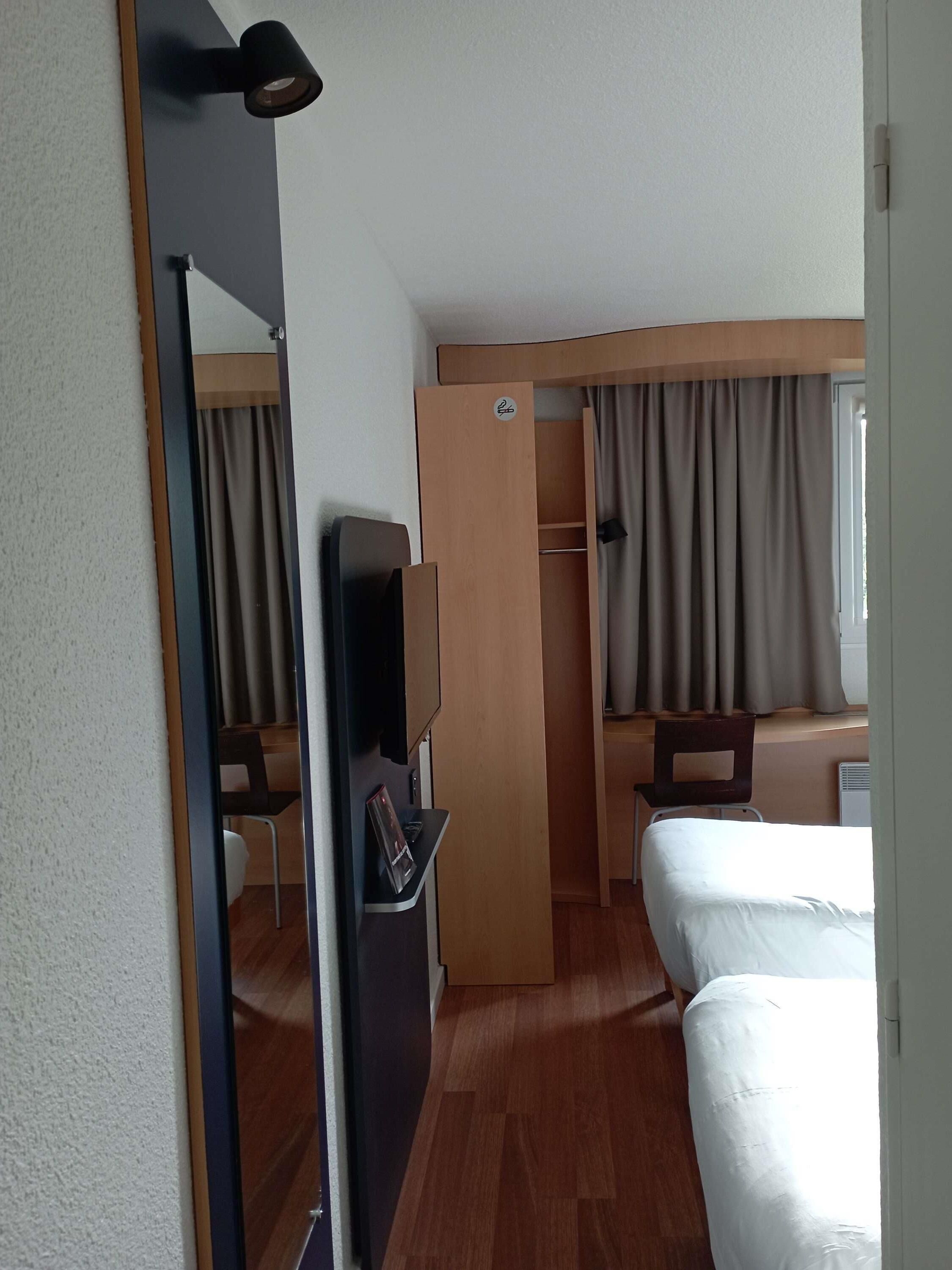 Une chambre d’hôtel comprenant un lit, un bureau, une chaise, une télévision et une armoire.