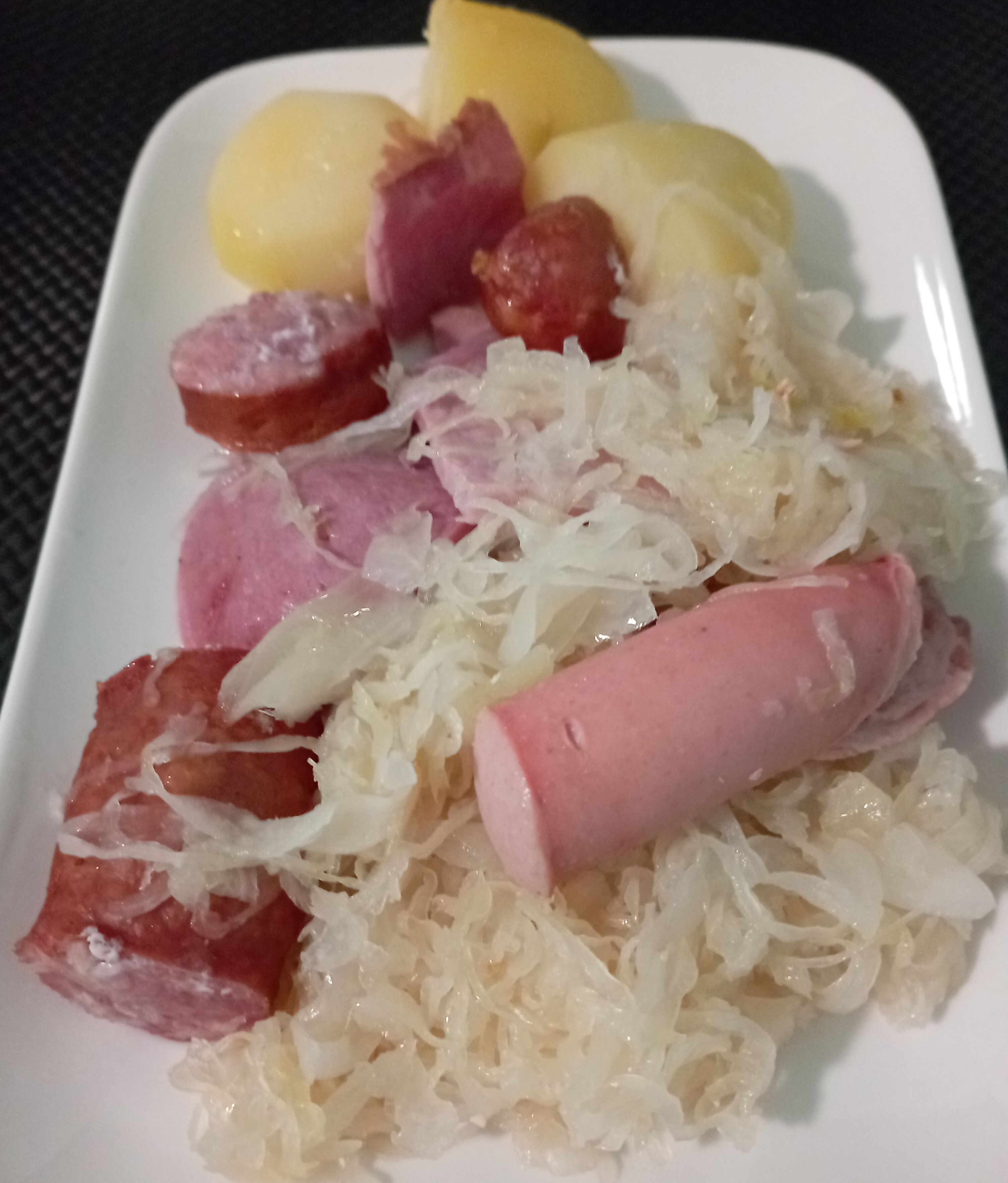 Un plato con chucrut, salchichas en rodajas y patatas hervidas.