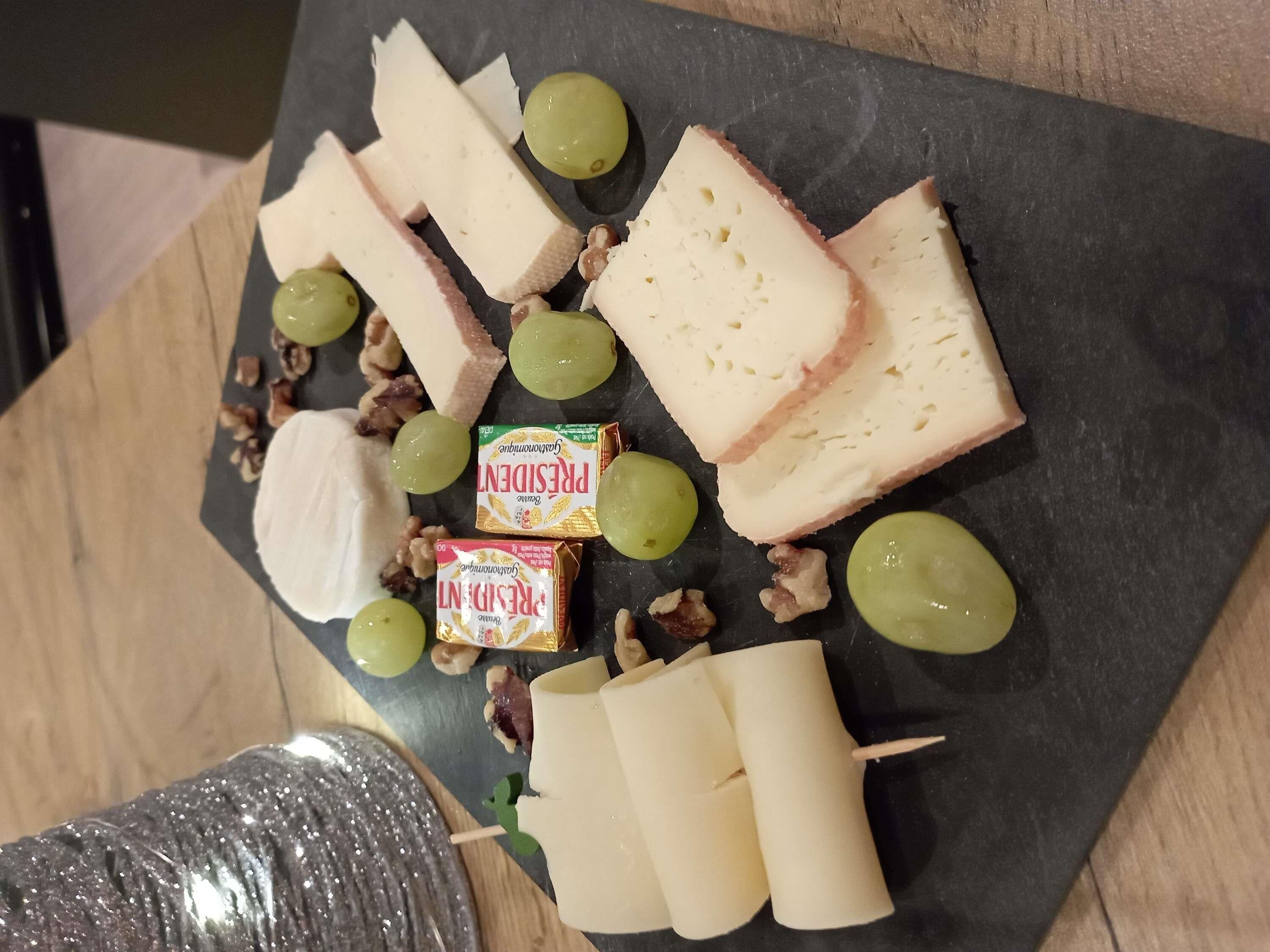 A cheese board with various cheeses, grapes, nuts, and crackers on a slate board.