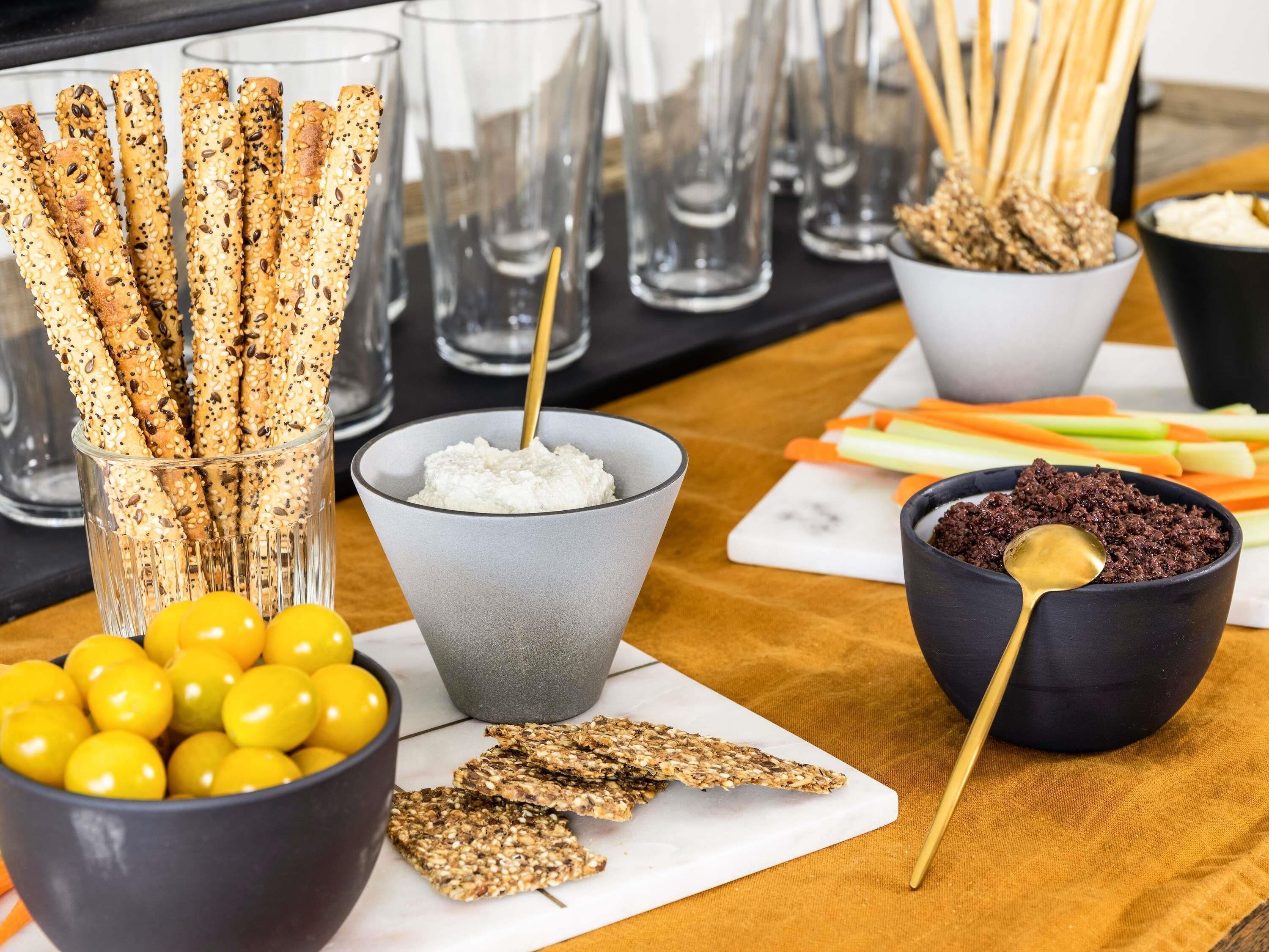 Une table sur laquelle on trouve divers aliments, notamment des gressins, du fromage, des olives et des crackers.