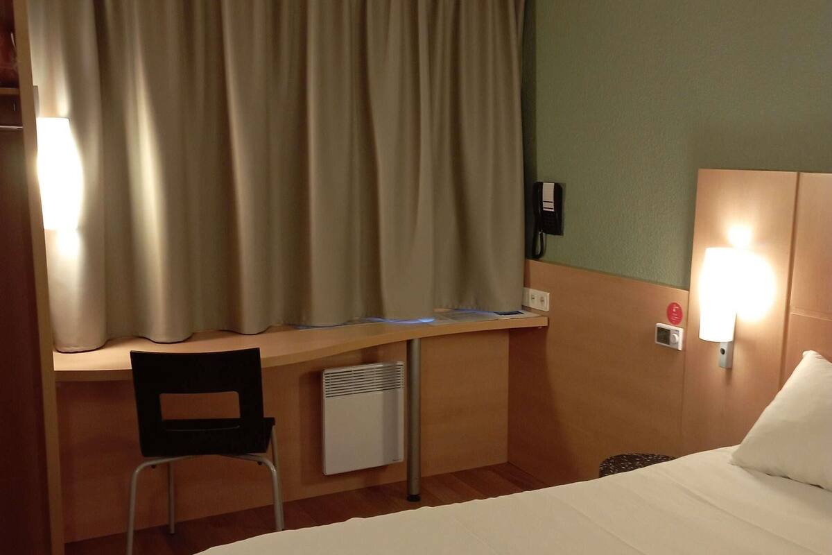 A hotel room with a bed, desk, chair, and a telephone.