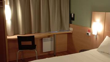 A hotel room with a bed, desk, chair, and a telephone.