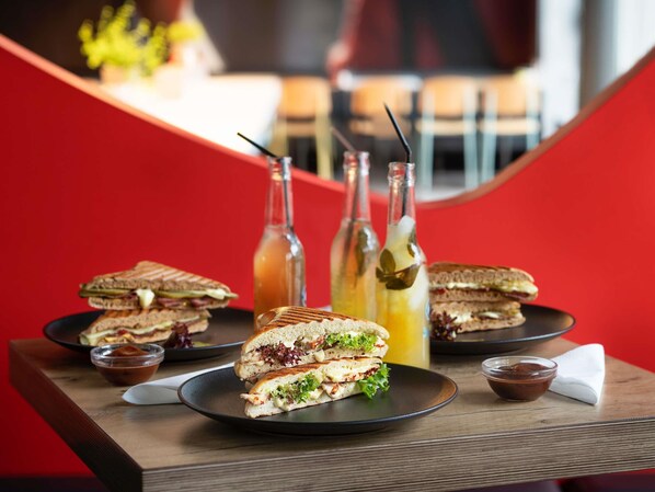 A sandwich on a plate with a napkin and a small bowl, set on a table with a red background. - Ibis Fourmies (Fourmies)