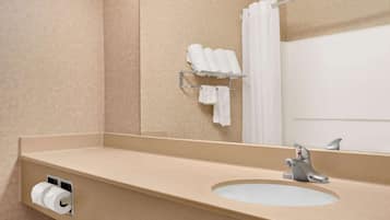 Une salle de bain avec un comptoir de couleur beige, un lavabo, un miroir, un porte-serviettes avec des serviettes et un porte-rouleau de papier toilette.