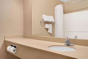 Un baño con encimera color beige, lavamanos, espejo, toallero con toallas y dispensador de papel higiénico.