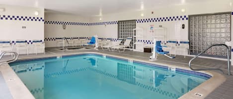A clean indoor swimming pool with blue and white tiled walls, multiple lounge chairs, and a clear pool area.