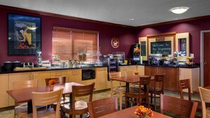 Una cocina de hotel con armarios de madera, una estación de café y una barra para el desayuno.