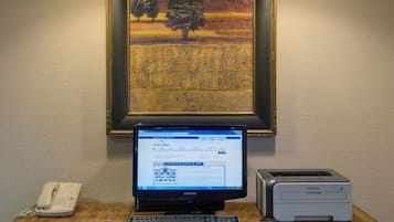 Un bureau en bois avec un ordinateur portable, une imprimante Brother et un téléphone. Une chaise rouge est placée devant le bureau. Un tableau encadré est accroché au mur, au-dessus du bureau.