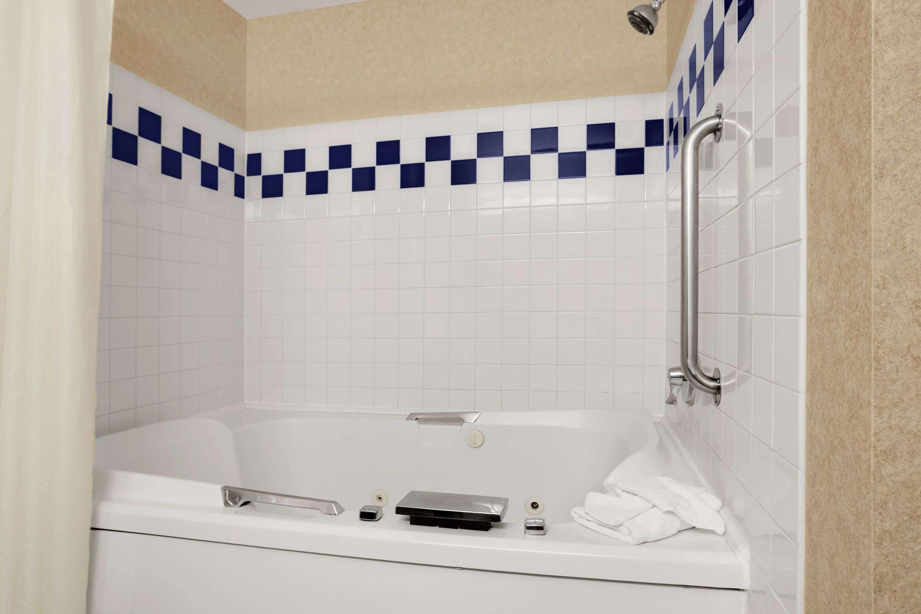Un baño moderno con una bañera blanca, un cabezal de ducha de mano y una barra de apoyo.