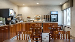 A restaurant with wooden furniture, a counter with a coffee machine, and a refrigerator with beverages. - Atherton Park Inn & Suites (Redwood City)