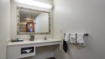 Un bagno con uno specchio grande, un lavandino, un portasciugamani con asciugamani e un piccolo ripiano con articoli da toilette.