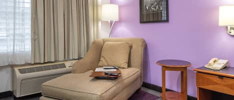 A hotel room with a single sofa, a small round table, a telephone, a lamp, and a framed picture on the wall.