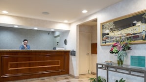 A reception desk with a wooden panel, a mirror above it, and a welcome sign. - Atherton Park Inn & Suites (Redwood City)