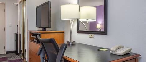 A hotel room with a wooden desk, a television, a lamp, a telephone, and a mirror.