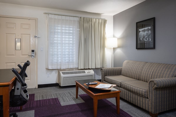 A hotel room with a sofa, a table with a remote control, a treadmill, and a window with curtains.
