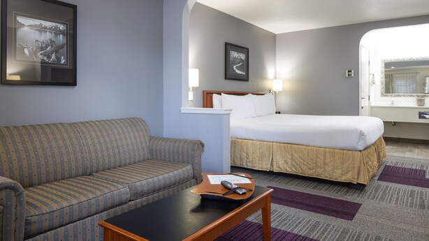 A hotel room with a bed, a sofa, a table, and two framed pictures on the wall. - Atherton Park Inn & Suites (Redwood City)