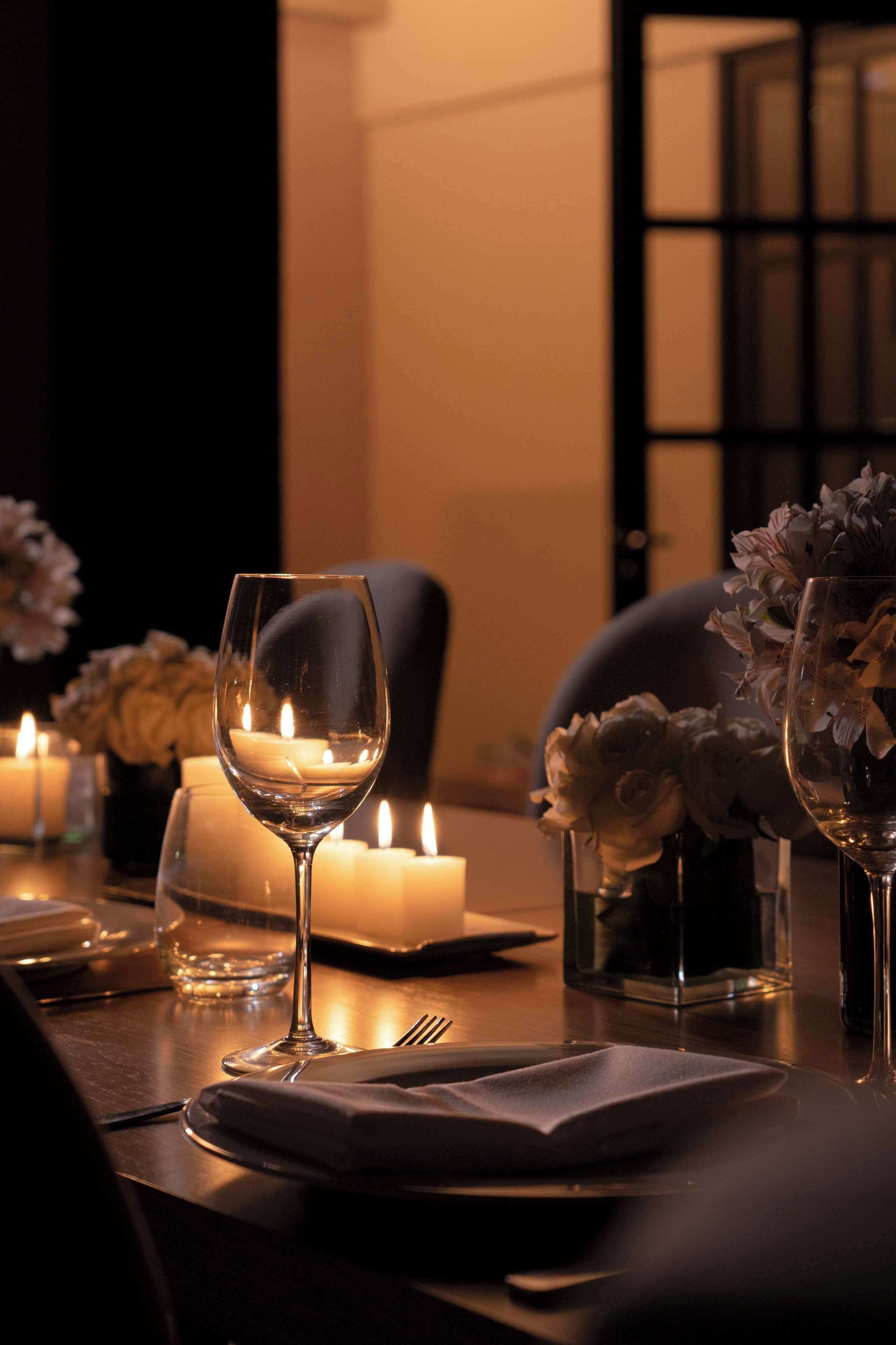 A dimly lit table set for dining with candles, glasses, and floral arrangements.