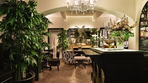 Vestíbulo de hotel con suelo de espiga, un candelabro, plantas en macetas y una zona de bar.