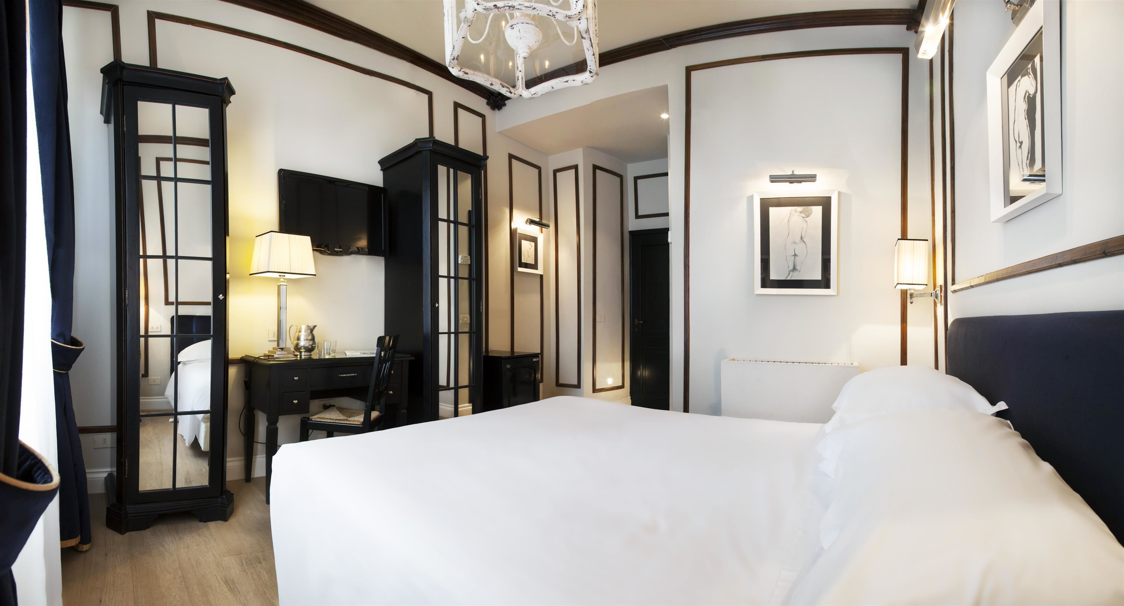 A hotel room with a large bed, a desk with a chair, a wardrobe, and a mirror.