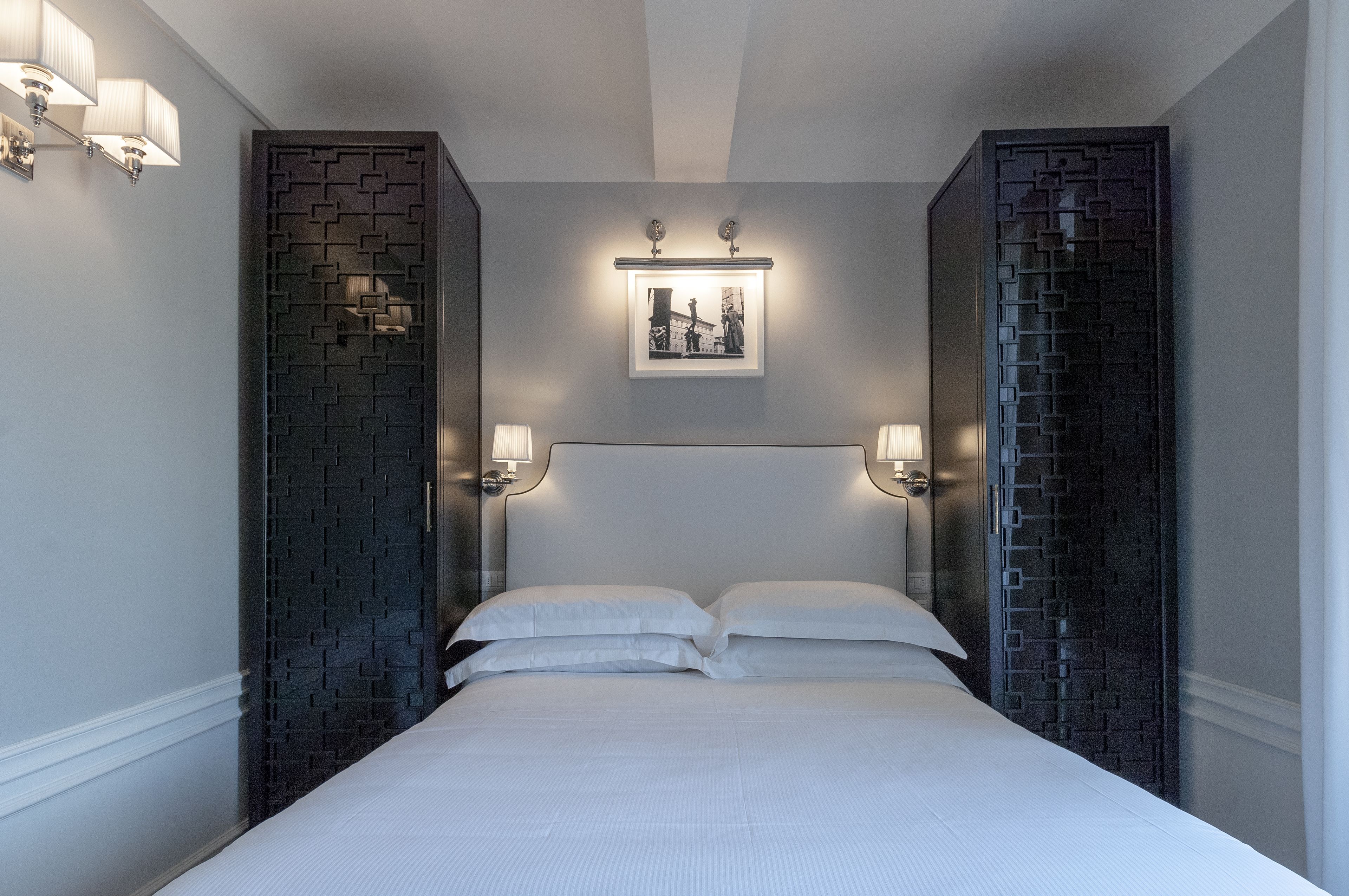 A modern bedroom with a large bed, two wall-mounted lamps, and a framed picture above the bed.