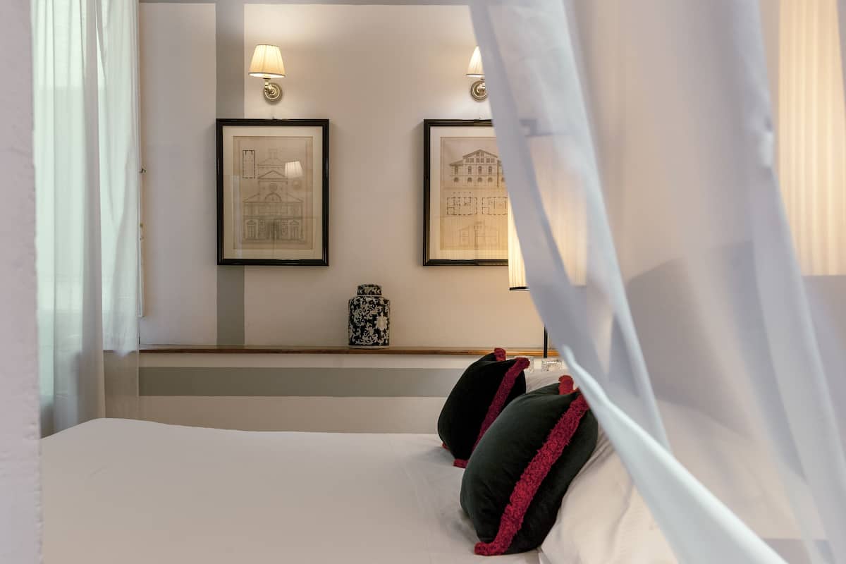 A hotel room with a bed, two framed pictures on the wall, a vase, and a nightstand.