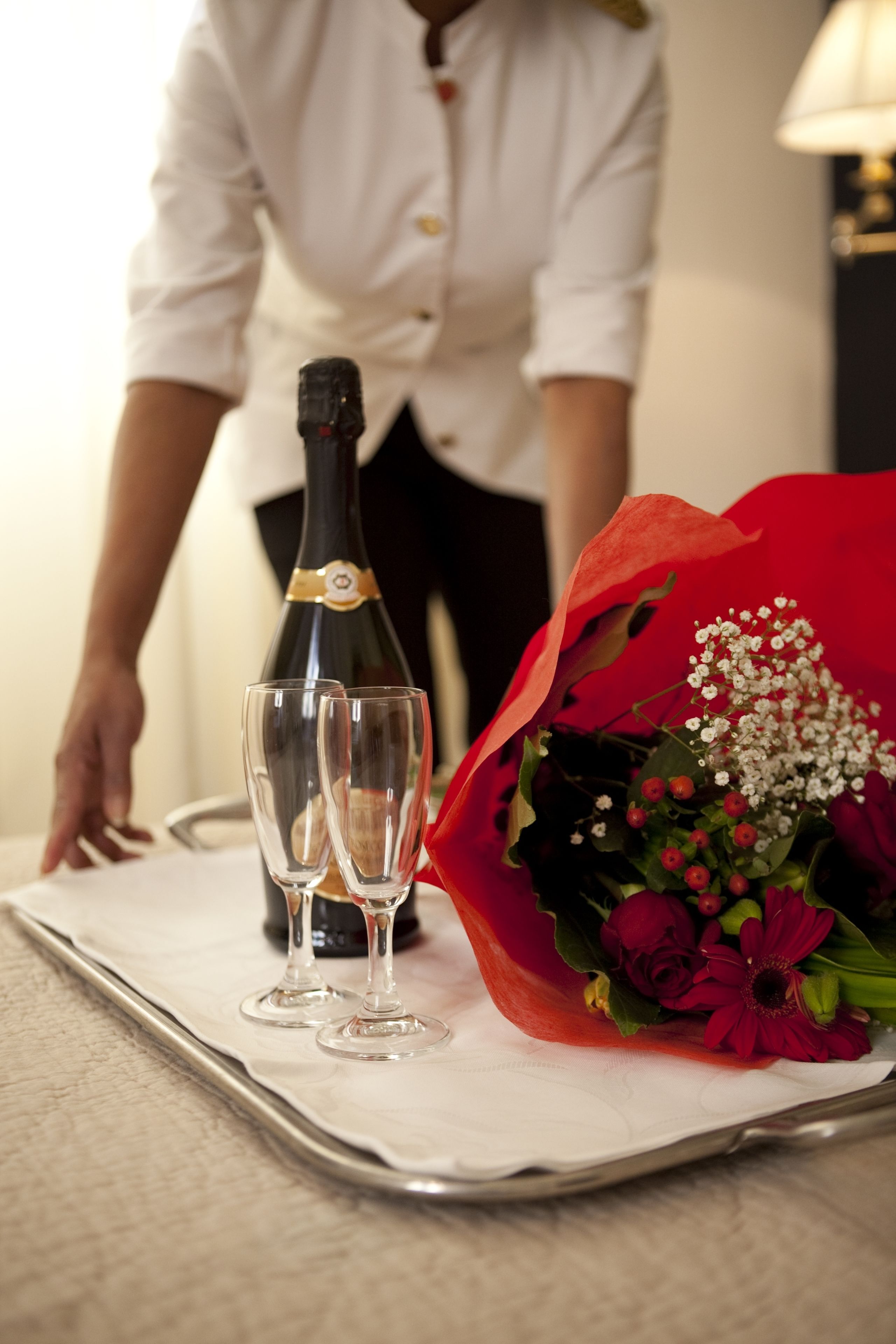 A tray with a bottle of champagne and two glasses, and a red floral arrangement.