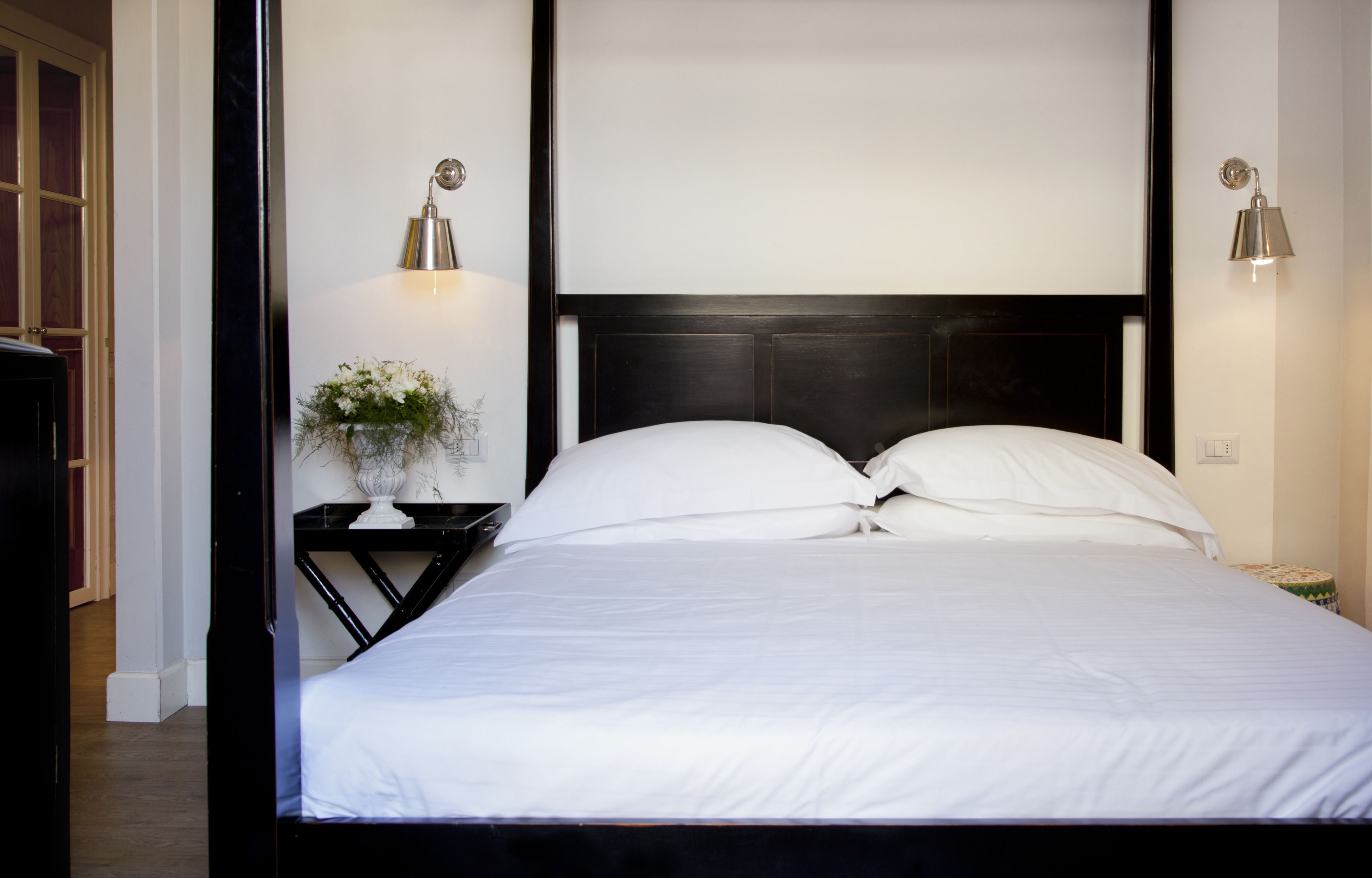A neatly made bed with white linens, a dark headboard, and two wall-mounted lamps on either side.