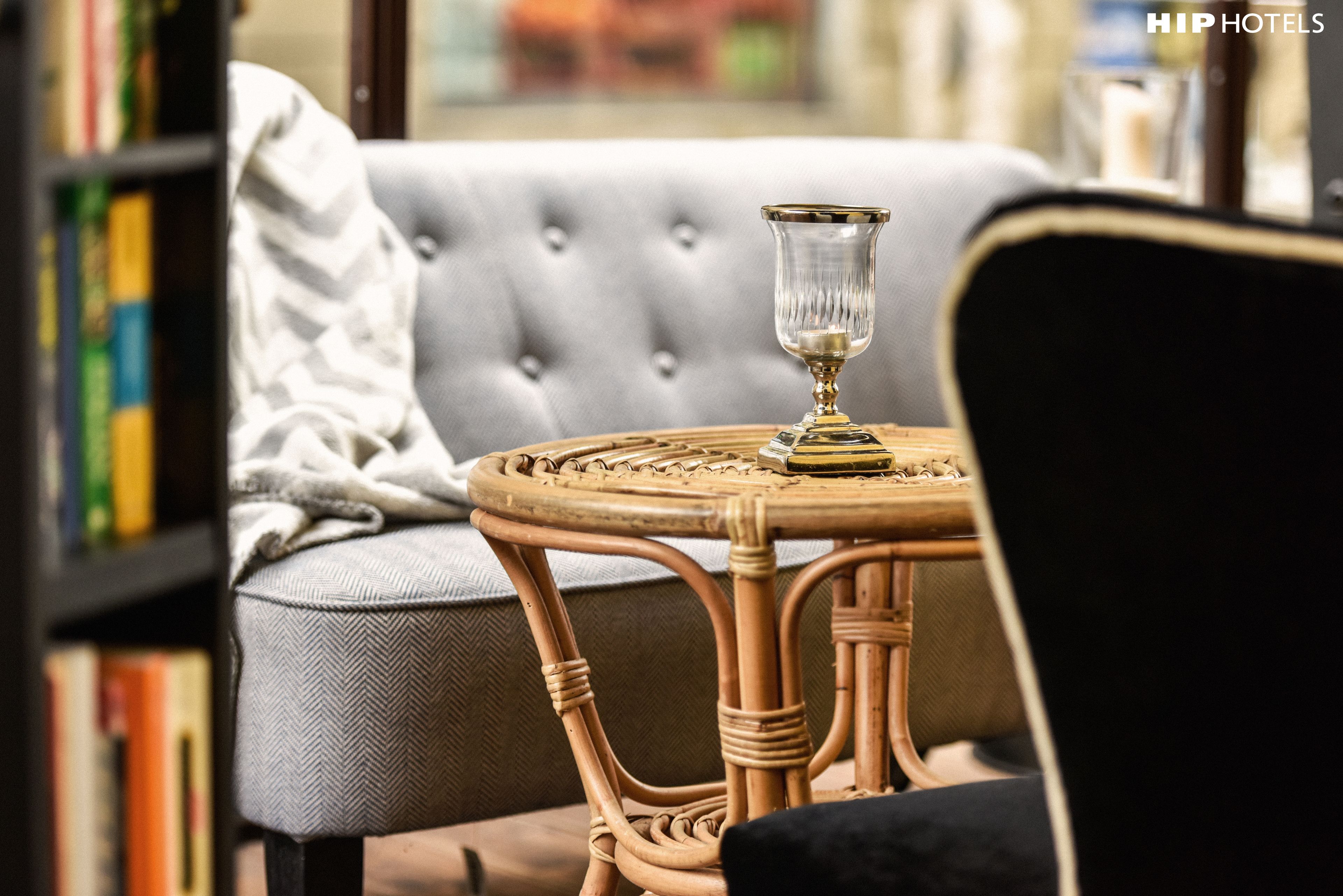 A wicker table with a glass on it, a grey sofa, and a bookshelf in a room.