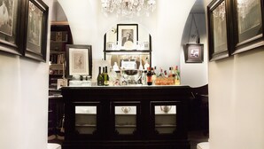 Una zona de bar con un mostrador de madera oscura, cuadros en las paredes y una lámpara de araña colgando.