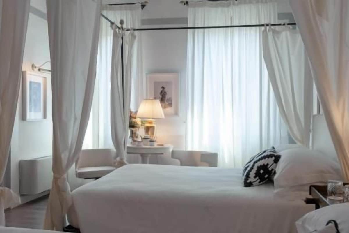 Una habitación de hotel con una cama, una mesita de noche, una lámpara y cortinas.