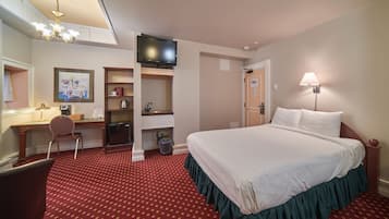 A hotel room with a large bed, a desk with a chair, a television, and a red carpeted floor.