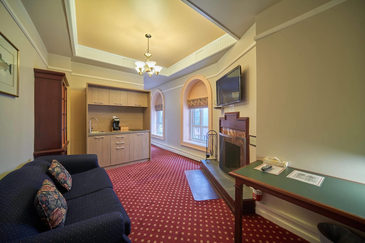 A room with a sofa, a desk, a television, a kitchen area, and a staircase.