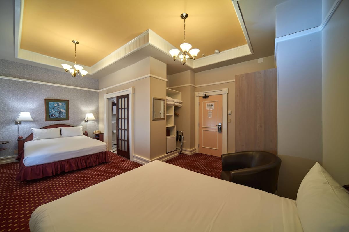 A hotel room with a large bed, two bedside lamps, a chandelier, a wooden wardrobe, and a chair.