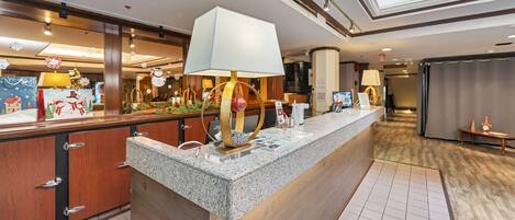 A hotel reception area with a marble counter, wooden cabinets, and a large window above.