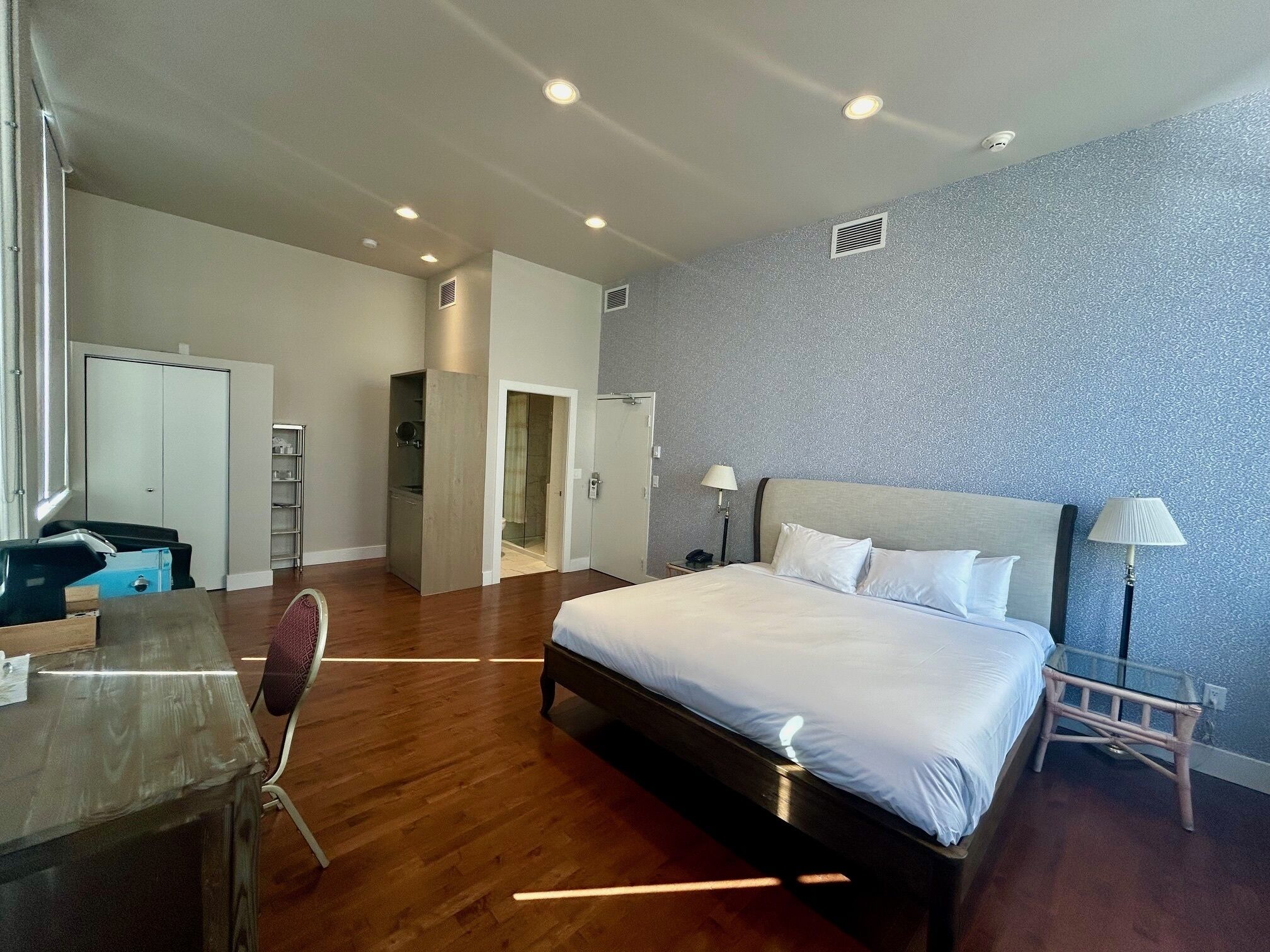 A modern hotel room with a large bed, a desk, a wardrobe, and a shower area.