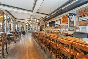 A bar area with wooden bar stools, a long counter, and a brick wall. - Bedford Regency Hotel, Trademark Collection by Wyndham (Victoria)
