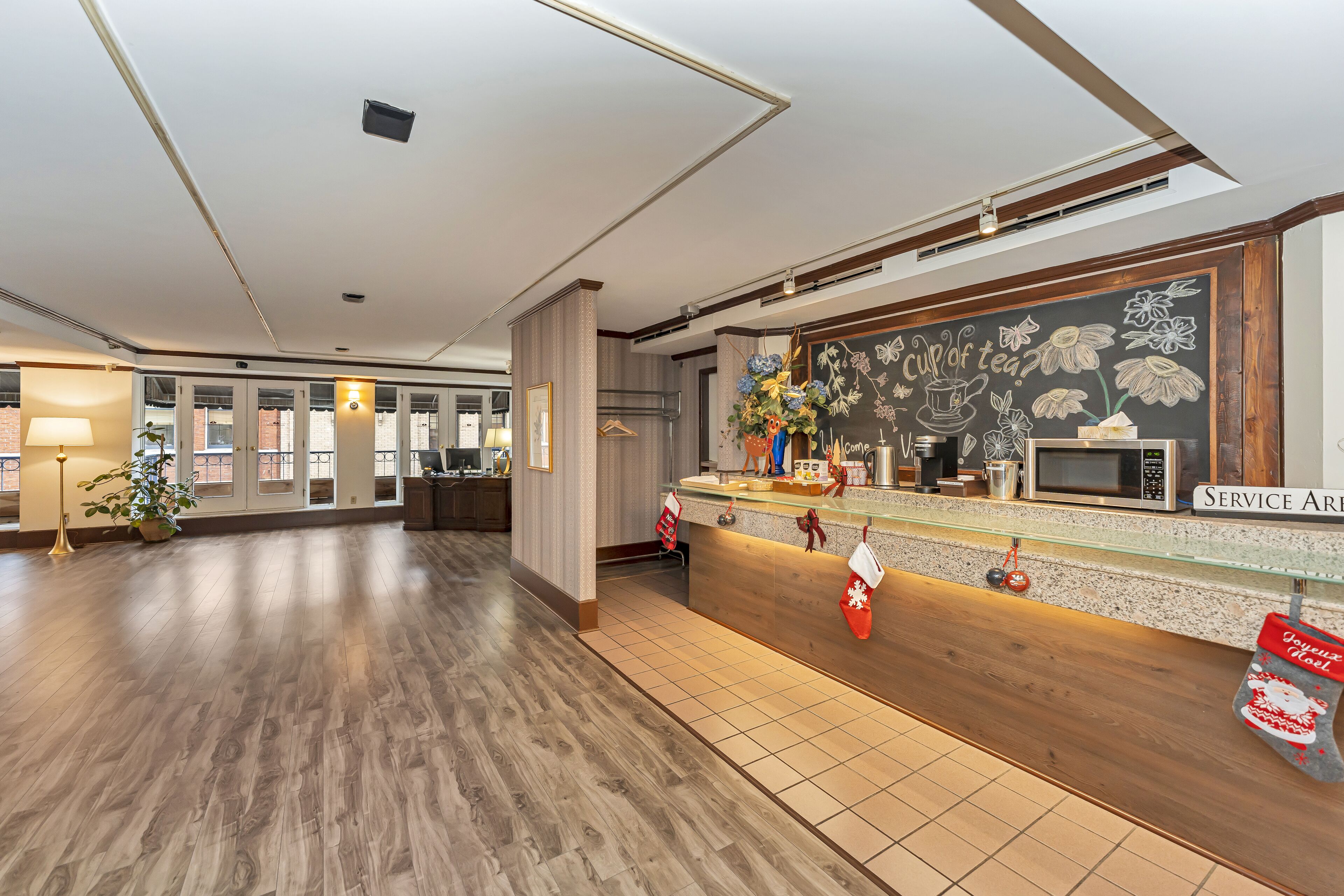 A spacious lobby with a wooden reception desk, a chalkboard with floral decorations, and a service area sign.