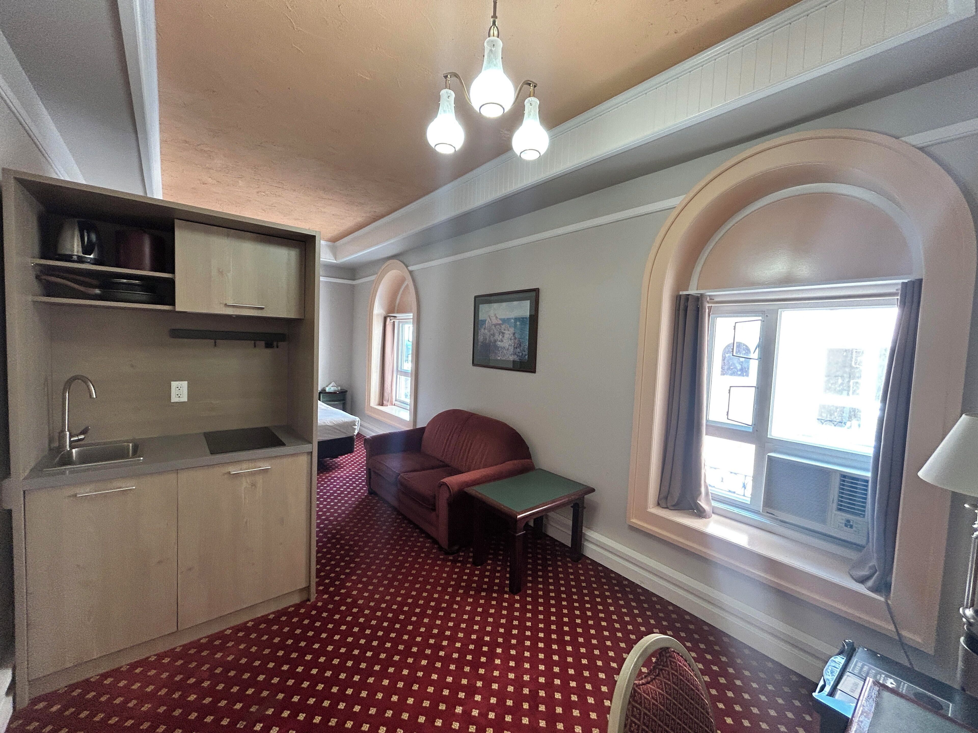 Een kamer met een kitchenette, een rood kamerbreed tapijt, een bank, een tafel en een raam met uitzicht.