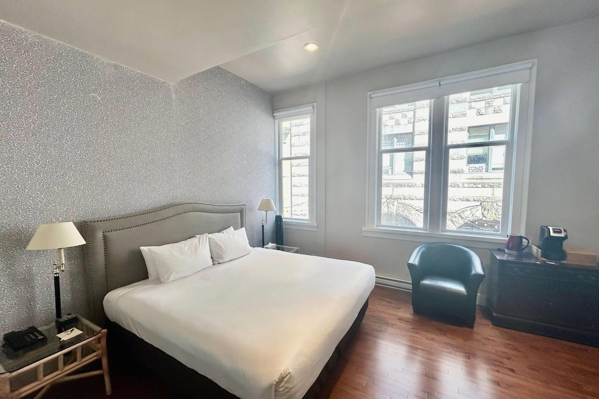 A hotel room with a large bed, a nightstand with a lamp, a chair, and a dresser.